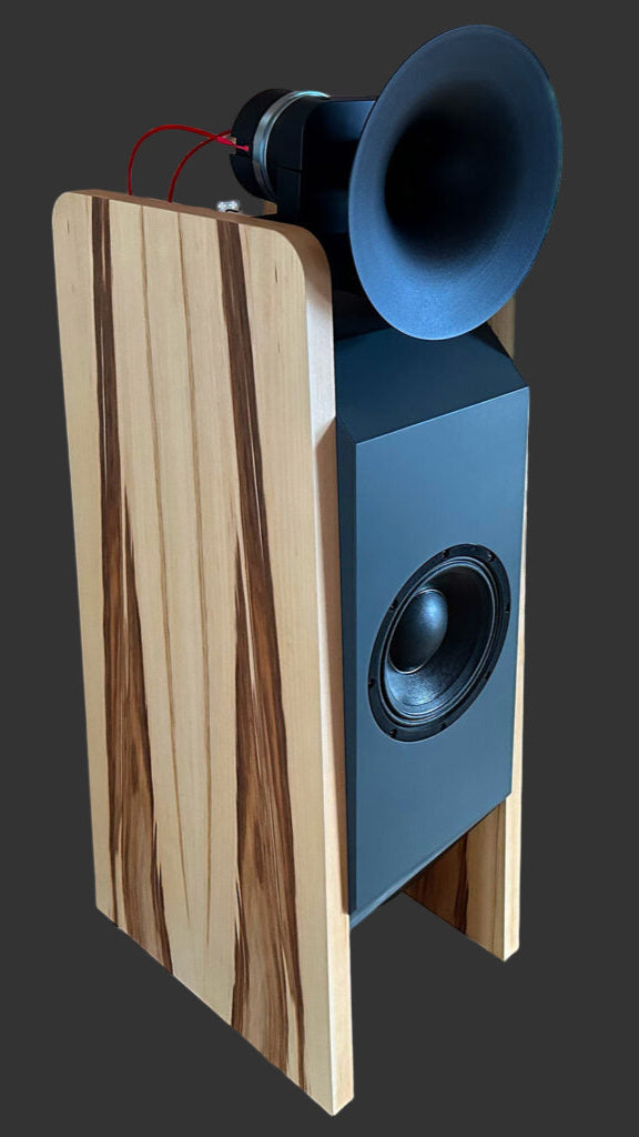 Wooden and black speaker on a wooden floor with audio equipment in the background